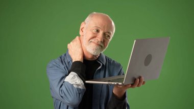 Yetişkin bir adam uzaktan muayene sırasında dizüstü bilgisayar tutarken boyun ağrısı çeker. Yeşil ekran arka planı çevrimiçi iletişim için profesyonel bir kurulum öneriyor.