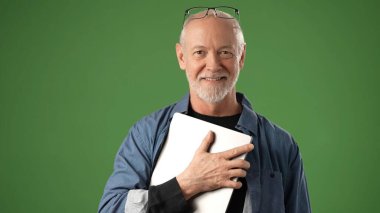 Üst düzey bir adam dizüstü bilgisayarı yakın tutarken sıcak bir şekilde gülümser. Yeşil ekran çeşitli duyurular veya ürün promosyonları için sağlam bir arkaplan sağlar.