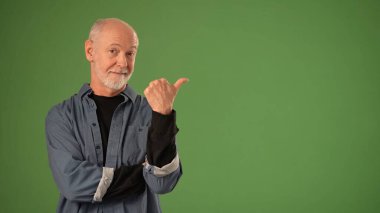 Olgun bir adam sert yeşil bir ekranın önünde durur, başparmağıyla hareket ederken neşeli bir yüz ifadesi sergiler. Ürün duyurusu için hazır görünüyor..