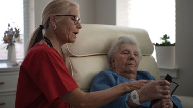 Bir bakıcı, aydınlık ve rahat bir oturma odasında, aydınlık ve rahat bir oturma odasında, yaşlı bir kadına yardım eder..