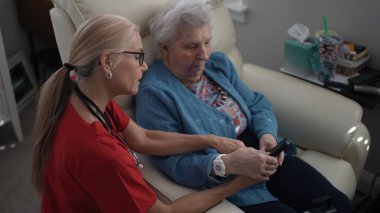 Bakıcı, yaşlı bir kadınla iletişim kurar ve ona sağlık merkezinde bir cihaz ile yardımcı olur. Ayarlama hafıza bakımını ve bağlılığı teşvik eder.