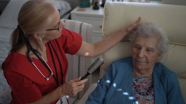 Bakıcı, yaşlı bir kadının saçını bir sağlık merkezinde nazikçe tarar ve öğleden sonra rutin bir bakım sırasında sıcaklığı ve bağlantıyı teşvik eder..