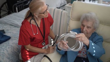Bakıcı, yaşlı bir kadının saçını hafifçe tarar, güneşli bir öğleden sonra sıcak bir oturma odasında rahatlık ve bakım sağlar..