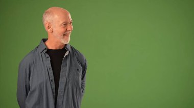 Olgun bir adam yeşil bir zemine karşı gururla durur. Sıcak bir gülümseme ve kendine güvenen bir duruş sergiler. Ürün duyurusu için mükemmel bir duruştur..