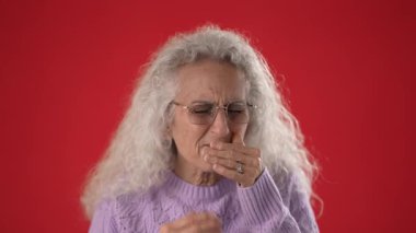 50-60 yaşlarında, beyaz, kıvırcık saçlı ve gözlüklü orta yaşlı bir kadın, parlak kırmızı bir ortamda, rahat mor bir kazak giyen, çeşitli duygular sergiliyor..