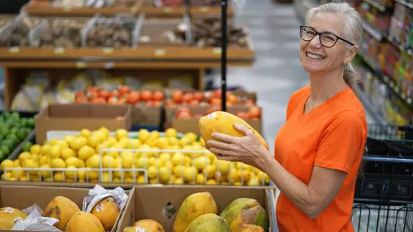 Gülümseyen mutlu olgun bir kadının portresi markette papaya seçiyor..