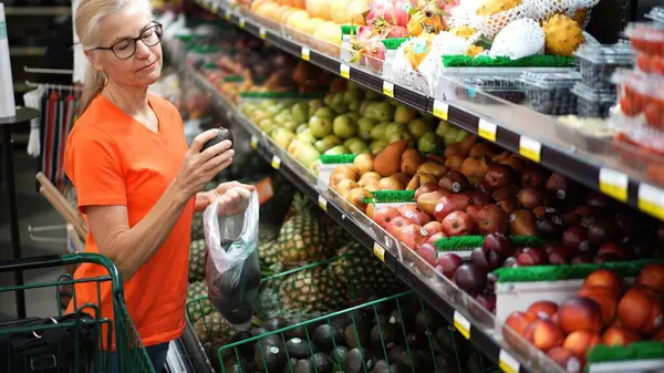 Mutlu, olgun bir kadın marketten taze avokado seçiyor..