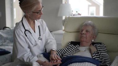 Bir hemşire, yaşlı bir kadına evinde nazik bir bakım sunarak, ziyaret sırasında rahatlık ve ilgi sağlar. Ortam sıcak ve destekleyici..