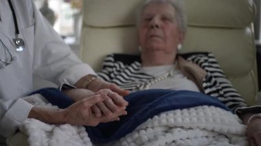 Yaşlı bir kadın evinde dinlenirken, bir sağlık görevlisinden şefkatli bir ziyaret alıyor, etkileşim sırasında konfor ve bakımı teşvik ediyor..