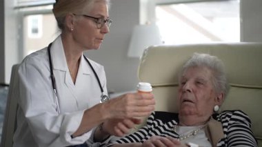 Bir sağlık uzmanı, ev ziyareti sırasında yaşlı bir kadına ilaç talimatı verir. Etkileşimde sağlık ve sağlık ihtiyaçlarına dikkat edilmesi vurgulanıyor.