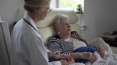 Yaşlı bir kadın evinde rahatça oturup, bir sağlık görevlisiyle sohbet ediyor. Sıcak bir atmosferde bir anlık bağ ve destek paylaşıyorlar..