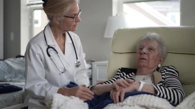 Bir hemşire, evinde yaşlı bir kadınla dikkatlice temas kurar, ziyaret sırasında tıbbi destek ve arkadaşlık sağlar, konfor ve bakımı teşvik eder..