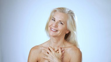 Kaplıcadaki olgun bir kadın mutluluğu yayar, içten gülümserken yumuşak beyaz bir arka plana karşı minnettarlığını ve memnuniyetini ifade eder..