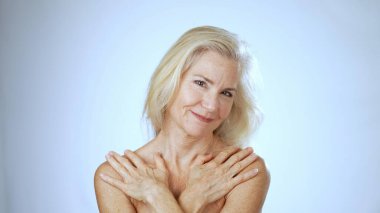 Neşeli olgun bir kadın kollarını kavuşturup huzurlu bir spa ortamında mutluluk saçarak poz verir. Parlak arka plan onun neşeli ifadesini arttırır..