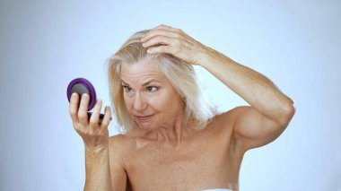 Olgun bir kadın, sakin bir spa ortamında saçlarını zevkle tarıyor. Arka plan parlak ve aydınlık. Neşeli ifadesini geliştiriyor..