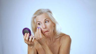 Olgun bir kadın spa 'da makyaj yaparken mutlu bir şekilde gülümser, kendini korumaya çalışır. Arka plan yumuşak ve beyaz, ışığı ve havayı güçlendiriyor..
