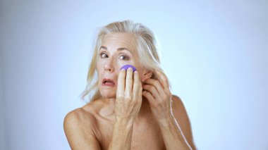 Olgun bir kadın spa 'da kendine bakmaktan zevk alır. Süngerle makyaj yapar ve gülümser. Parlak, rahatlatıcı bir atmosferde mutluluk yayar..