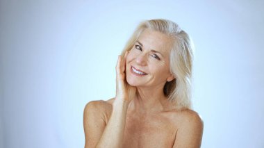 Mutlu, olgun bir kadın spa ortamında rahatlar, ışıl ışıl gülüşünü ve parıldayan tenini sergilerken sakin bir atmosferi ve beyaz arka planı takdir eder..