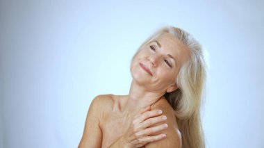 Mutlu, olgun bir kadın spa 'da rahatlarken gülümser. Huzurlu arka plan onun neşeli yüz ifadesini güçlendiriyor, bir anlık kişisel bakım sergiliyor.