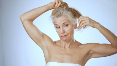 Mutlu, olgun bir kadın saçlarını zarif bir şekilde atkuyruğu şeklinde parlak bir kaplıca ortamında toplarken gülümsüyor. Sıcak ortam onun gevşemiş davranışlarını arttırıyor..