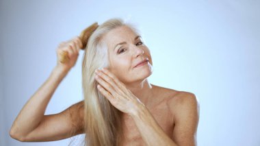 Uzun saçlı mutlu bir kadın, sakin bir spa ortamında saçlarını tarar, neşe ve rahatlama yayar. Yumuşak beyaz arka plan rahatlatıcı atmosferi güçlendirir.