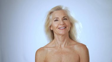 Olgun bir kadın huzurlu bir spa ortamında gevşer, neşeli bir şekilde gülümser, yüz hatlarını aydınlatır, huzur ve mutluluğu somutlaştırır..