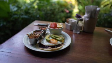 Orta yaşlı bir kadın bir kafe masasında oturmuş, yeşilliklerle çevrili lezzetli bir yemeğin tadını çıkarıyor. Dijital göçebe olarak iş tatilinin tadını çıkarıyor..