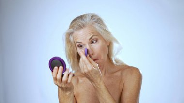 Olgun bir kadın gülümserken makyaj yapar. Parlak, sakin bir spa ortamında bir anlık özgüven ve rahatlamayı kucaklar..