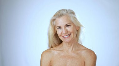 Sakinleştirici bir spa ortamında, olgun bir kadın gülümserken mutluluk yayar, temiz beyaz bir arka plana karşı sağIık ve sükunet duygusu gösterir..