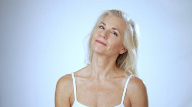 Olgun bir kadın mutlu bir şekilde gülümser, gençleştirici spa tedavisi sırasında mutluluğunu gösterir. Serin beyaz arka plan rahatlatıcı atmosferi arttırır..