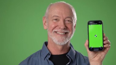 Arkadaşça gülümseyen orta yaşlı bir adam elinde yeşil ekran bir futbol topu grafiği olan bir akıllı telefon tutuyor. Arka plan canlı bir yeşildir..