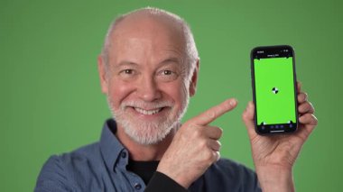 Neşeli orta yaşlı bir adam akıllı telefonuna doğru hareket eder, canlı yeşil ekran arka planına karşı interaktif bir futbol uygulamasının altını çizer.