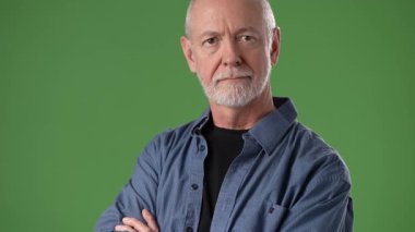 Olgun bir adam, kollarını parlak yeşil bir ekran arkaplanına kavuşturarak güvenle ayakta duruyor. Portrede sakin ve dengeli bir tavır sergiliyor..