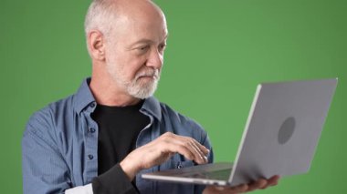 Gri sakallı olgun bir adam, elinde bir dizüstü bilgisayarla parlak yeşil bir ekrana karşı duran bir seyirciyle karşılaşır. Arkadaş canlısı ve bilgilendirici görünüyor..