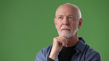 Sakallı ve kısa saçlı olgun bir adam elini yeşil bir zemine dayayıp düşünceli bir şekilde poz verir..