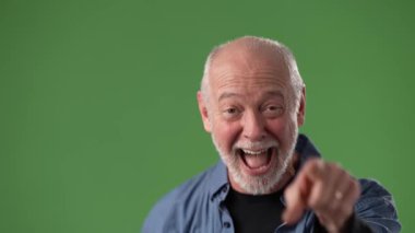 Orta yaşlı bir adam yeşil bir ekranın önünde dururken neşeli tavırlarını sergileyerek geniş bir gülümseme sergiliyor. Mavi gömleği dost canlısı kişiliğini tamamlıyor..