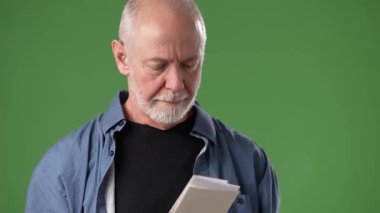 Olgun bir adam elinde sağlam yeşil bir geçmişi olan bir belgeyle güvenle ayakta duruyor. İfadesi ciddiyet ya da tefekküre işaret ediyor..