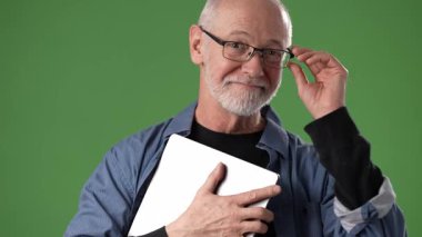 Olgun, orta yaşlı bir adam göğsüne yakın bir tablet tutarak canlı yeşil bir perde arkasına sıcak bir şekilde gülümsüyor..