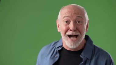 Olgun bir adam ellerini parlak yeşil bir arka planda tutarak yüzünü kapatarak bir dizi duygu sergiliyor, dokunaklı bir yansıma anı yakalıyor..