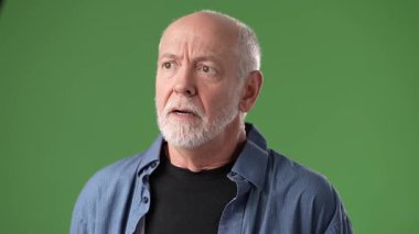 Sakallı orta yaşlı bir adam yeşil ekranın önünde güçlü duygular ifade eder. Yüzündeki ifade, o anda yoğun ve tutkulu bir ifade sergiliyor..