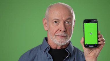 Sakallı olgun bir adam başparmağını kaldırırken geniş bir gülümseme sergiliyor. Elinde yeşil bir arka plan gösteren, coşku ve pozitiflik saçan bir akıllı telefon var..