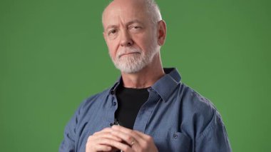 Olgun, orta yaşlı, gözlüklü bir adam parlak yeşil bir arka plana karşı düşünceli bir şekilde poz verir. İfadesi tefekkür ya da entrika olduğunu gösteriyor..