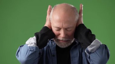 Gri saçlı ve sakallı olgun bir adam, kulaklarını kapatarak ve bağırarak düş kırıklığını açıkça gösterir..