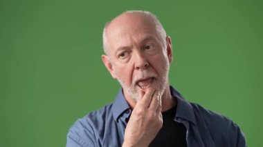 Gri sakallı olgun bir adam parlak yeşil bir ekranın önünde durarak derin düşünceler içinde belirir. İfadesi, tefekkür ve merakı ifade eder..