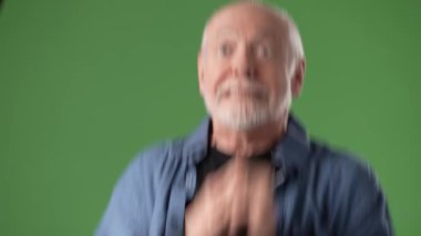 Gri saçlı ve sakallı olgun bir adam ellerini canlı yeşil bir zemine yapıştırarak keyifli bir anı işaret ediyor..