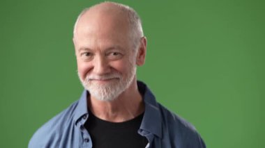 Orta yaşlı, sakallı ve arkadaş canlısı bir adam, yaratıcı projeler veya video prodüksiyonları için uygun yeşil ekran arka planına karşı duruyor..