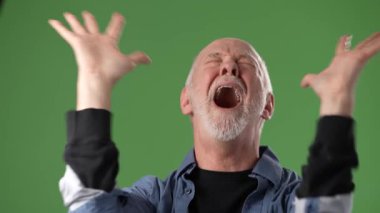 Orta yaşlı bir adam tutkulu bir şekilde ellerini kaldırır, çeşitli duygular gösterir, yaratıcı amaçlar için canlı yeşil bir ekrana karşı kurulur..