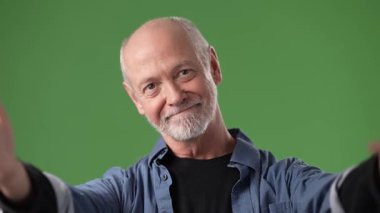 Orta yaşlı bir adam yeşil bir perde arkasında kendini kucaklarken sıcak bir şekilde gülümsüyor. Çevre aydınlık ve neşeli..