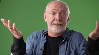 Kısa sakallı ve yüzünde gülümseme olan olgun bir adam yeşil bir ekrana karşı duruyor. Sohbete dalmış gibi görünüyor, el hareketleriyle..