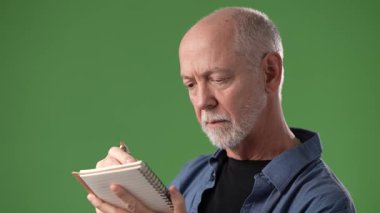 Olgun bir adam elinde bir defter tutarken, parlak yeşil bir ekranın önünde dururken, yaratıcı ifade ve fikirlere hazır bir şekilde gülümser..